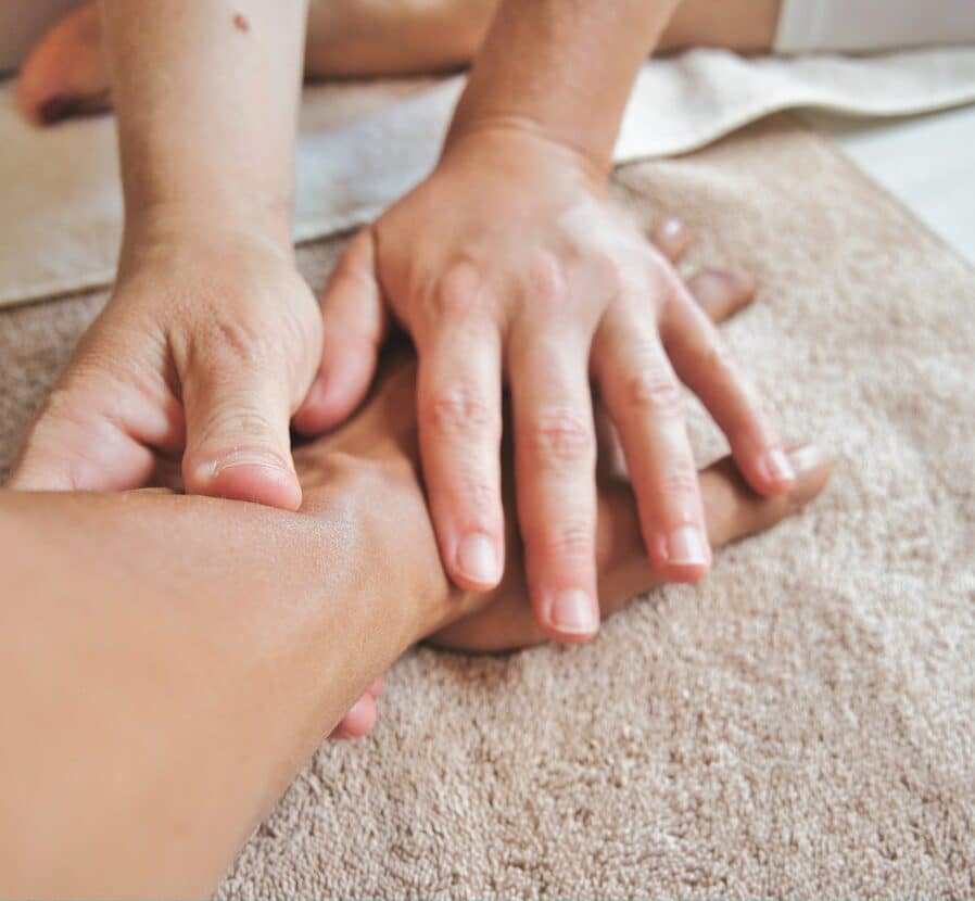 Gros plan d'une personne recevant un massage des mains ; les mains d'une personne pressent et massent doucement la main et le poignet d'une autre personne sur une serviette beige douce.